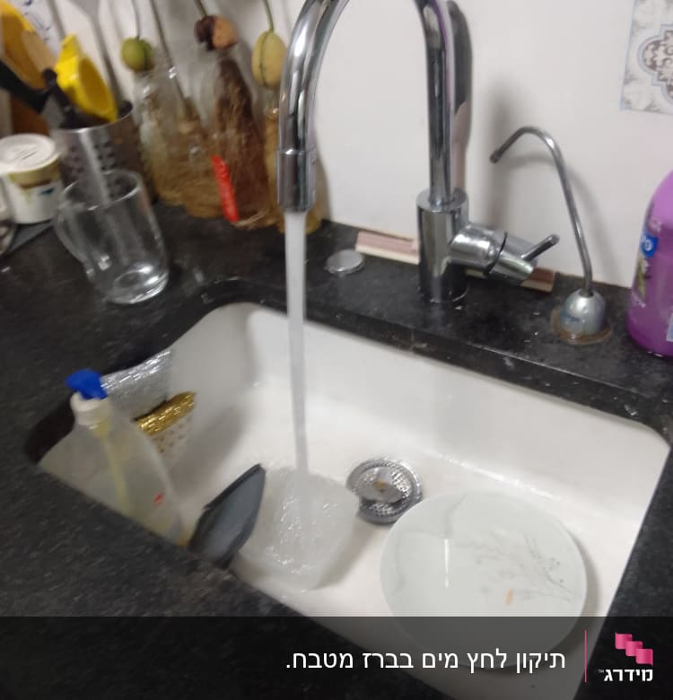 ברז מים זורמים בכיור מטבח עם כלים וסבון.